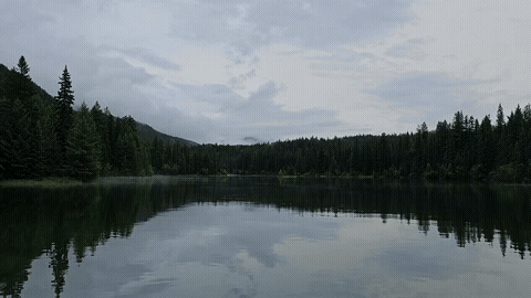 A still lake reflecting clouds and mountains at dusk"